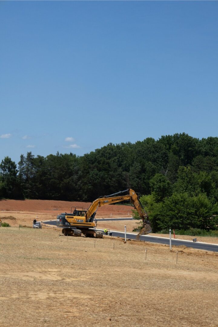 Excavator working on a construction site near a wooded area under a clear sky.