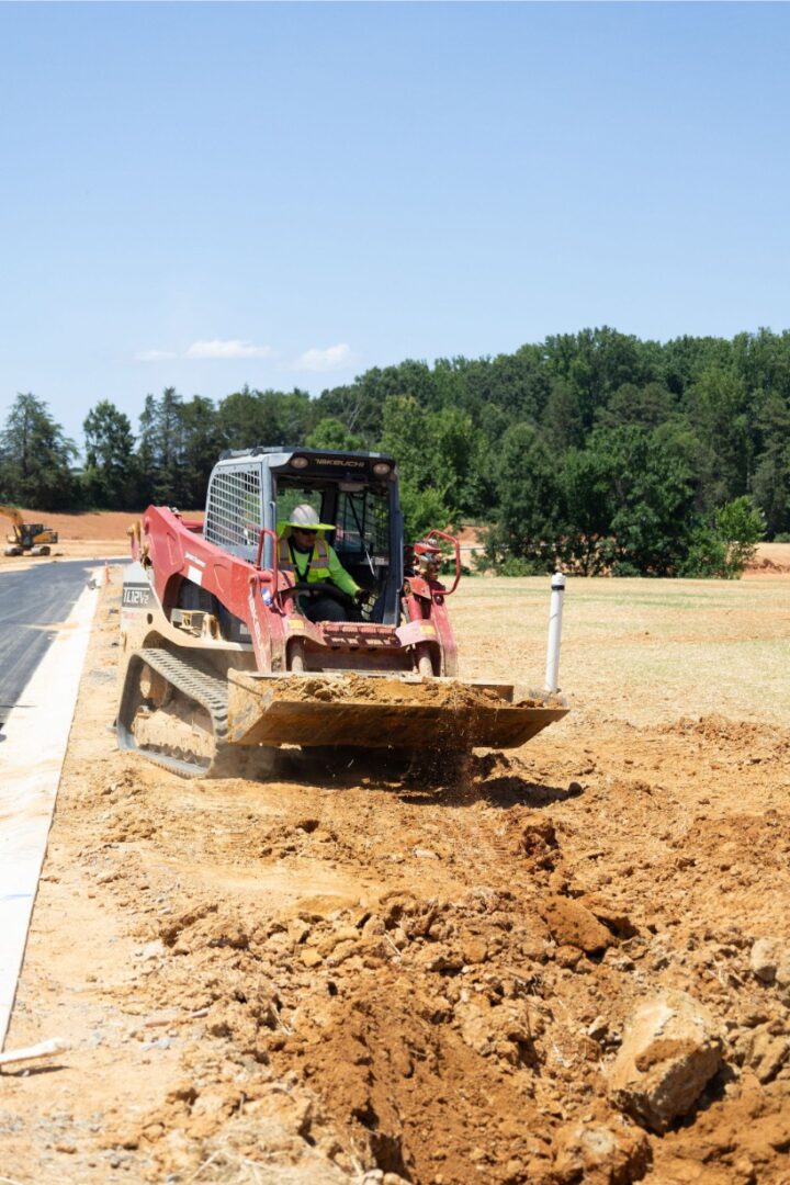 Construction worker operating bulldozer on a dirt site near a paved road.