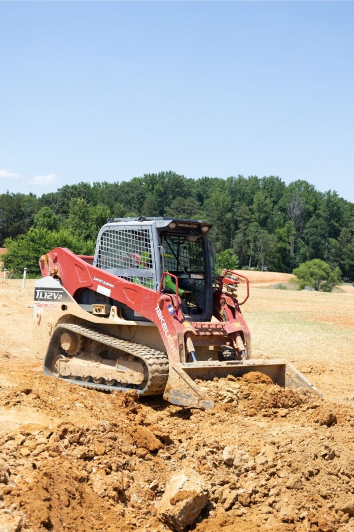 A red bulldozer working on a dirt field near a forest.