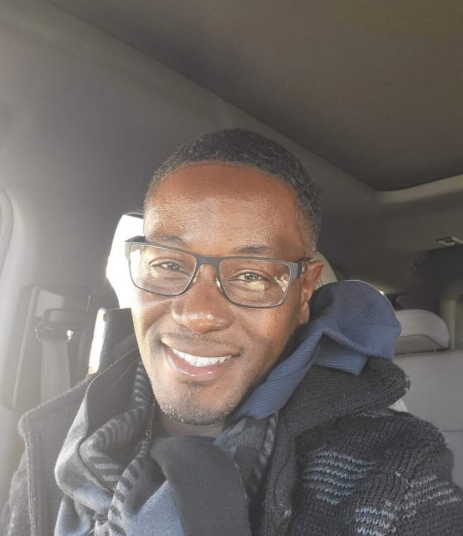 A smiling man wearing glasses inside a car.